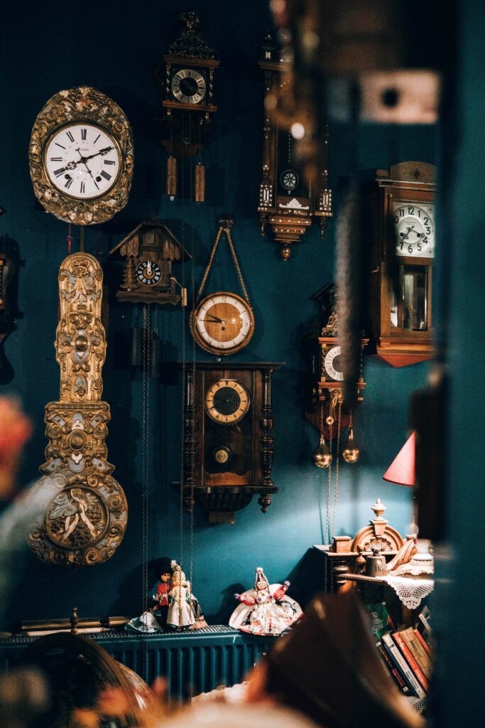 Several clockworks, wall clocks, antique looking, many different styles, hanging on a wall.